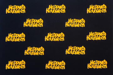 Halloween background. Orange confetti with text HAPPY HALLOWEEN and pumpkins on black paper background. Greeting card, festive backdrop for Halloween holiday. Flat lay, top view