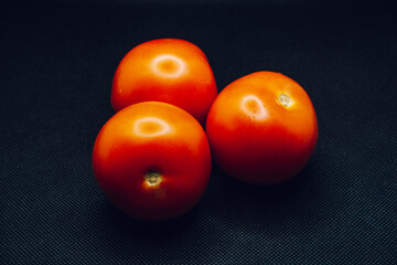 A trio of tomatoes on black background. Shallow focus, blur, red, 3, food prep, contrast, dark, lighting.