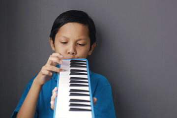 Boy playing blue melodeon musical instrument, melodica blow organ, pianica or melodion on dark gray...