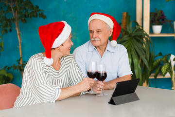 Elderly couple in a Santa's hat   drinking wine and using tablet and having video call with friends or relatives at home. Christmas at home