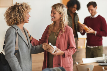 Side view at group of elegant adult people greeting each other and exchanging gifts while welcoming...