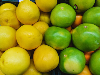 Fresh green and yellow pamelos (Latin Citrus māxima) are stacked on top of each other for sale in a hypermarket.