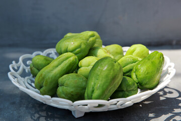 Fresh chayote fruits (Sechium edulis) on white plate and gray background
