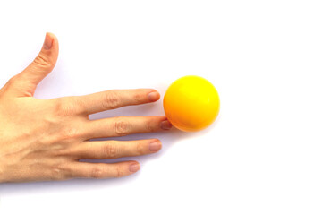 Fingers of a female hand touching a yellow plastic ball on a white background.
