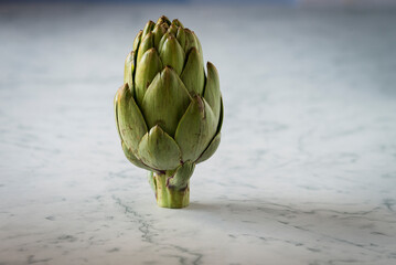 Obraz premium A green fresh artichoke on a marble counter