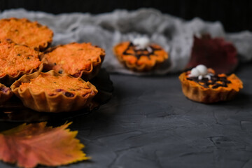 bright orange cupcakes in tartlets with a spider on background of gray web. next to autumn leaves. concept of Halloween