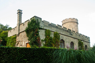 Stone building with battlements and towers covered with green ivy. Arched windows in the wall of the gray stone castle. Topiary garden in the Vorontsov Palace.