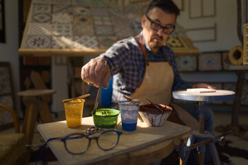 Artigiano decora a mano una piastrella di ceramica nella sua bottega