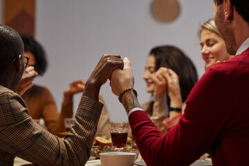 Multi-ethnic group of people holding hands in prayer at Thanksgiving dinner with friends and family, focus on foreground, copy space