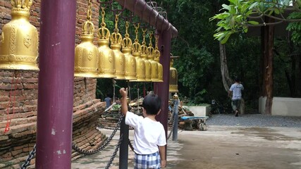 4K Asian cute child boy ring golden bells in local temple Thailand with happy smiling face. Buddhist activity and family travel concept.