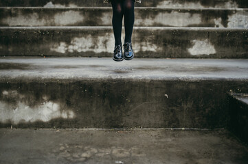Fototapeta na wymiar Visual storytelling detail on feet. Closeup little girl legs jumping on the stairs in a urban contest. Minimalism, lifestyle concept.