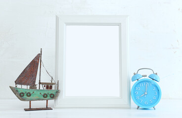 Image of white empty photo frame next to home plant over wooden table. For mockup, can be used for photography montage and text