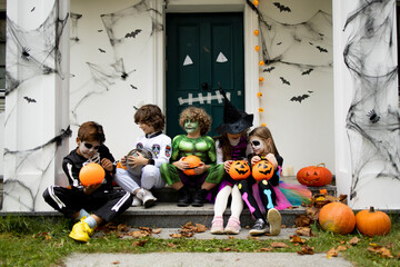 Fototapeta premium Group of trick-or-treating kids talking and sharing candies on a porch of a house during Halloween