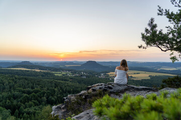 Junge Frau sitzt auf Steinen mit Blick zum Sonnenuntergang