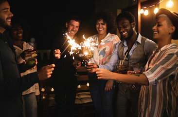 Happy friends celebrating with sparklers fireworks on 2021 new year's eve party - Soft focus on african man face