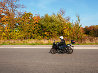 Motorcyclist in motion. Woman biker on a black motorcycle in traffic on a rural autumn road.