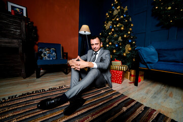 a businessman sits on the floor under a Christmas tree, waiting for Christmas night