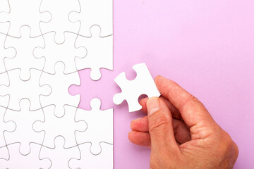 Hand placing white jigsaw puzzle piece. Horizontal composition with copy space.