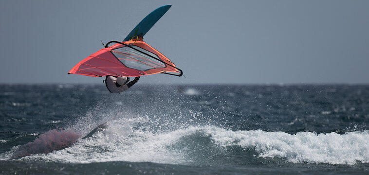 Windsurfer jumping over a big wave balancing in the sky