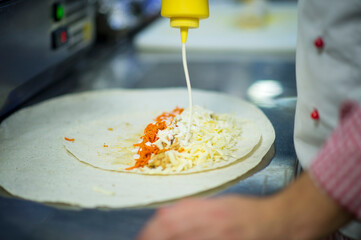 Chef making gyros on professional restaurant kitchen. Lavash bread (pita) with chicken, carrot and...