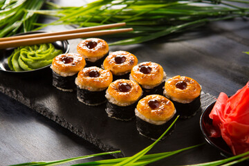 Set of baked sushi rolls with wasabi and ginger on black