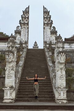 Beautiful Girl Standing With Open Arms On Stone Stairs To Gates Of Heaven In Pura Lempuyang Temple In Bali, Indonesia. Happy Young Woman Explore Ancient Architecture In Karangasem, Asia.