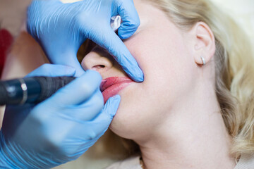 Cosmetologist applying permanent make up on lips