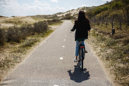 Full length image. Back view of a young girl walks single on bicycle on the road in sunny day time.