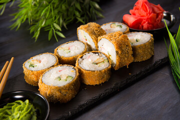 Set of baked sushi rolls with wasabi and ginger on black
