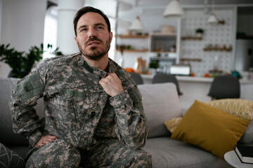 Fototapeta premium Depressed soldier sitting on sofa in living room. Young marine having PTSD.