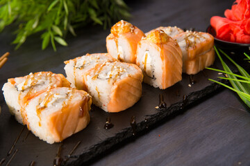 Set of baked sushi rolls with wasabi and ginger on black