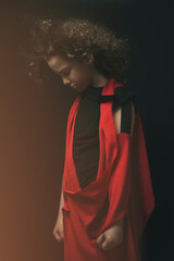 Portrait of a young boy with his eyes closed, in a black and red costume, wind blowing in his curly hair