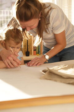 Beautiful woman cutting dress patterns in home with her little cute girl