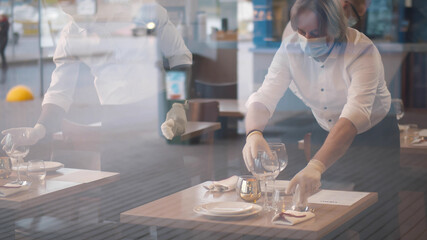Waiters in medical protective mask serving table in restaurant.