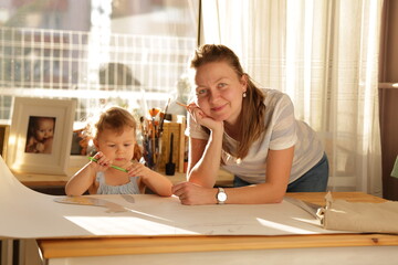 Beautiful woman cutting dress patterns in home with her little cute girl