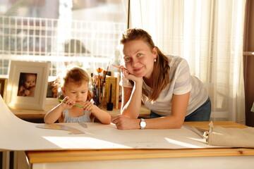 Beautiful woman cutting dress patterns in home with her little cute girl