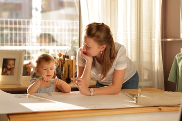 Beautiful woman cutting dress patterns in home with her little cute girl