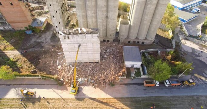 Kharkiv, Ukraine - 18 october 2020: a large excavator destroys an abandoned grain elevator building that was left after the demolition. He pushes the concrete structure. Aerial view from above