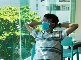 Asian man wearing medical face mask to prevent from covid 19 in room , sitting with tired posture.