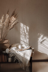 A shade from blinds on white wall and wooden table in the morning. A cup of coffee and an open book.