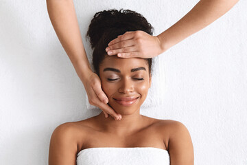 Top view of smiling black lady getting face massage