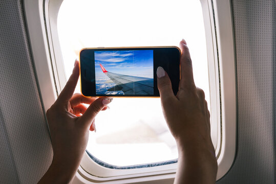 The passenger takes pictures on the plane. The girl takes a photo from the plane window on a mobile phone camera. Close-up of hands and smartphone screen. Travel and technology