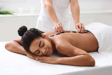 Obraz na płótnie Canvas African american woman having hot stone massage at spa