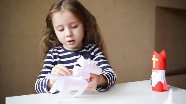 paper craft for kids. DIY toy Saint Nicholas and white horse for sinterklaas day. create art for children. girl glues horse.