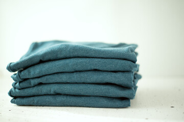 A stack of t-shirts of the same color on a light background. The minimalistic concept. Space for...