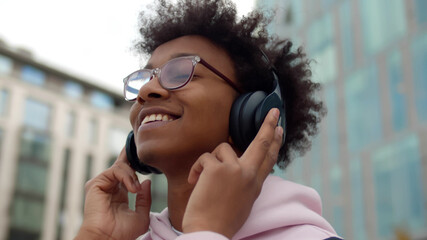 Close up of happy young afro man walking outdoors listening music in headphones