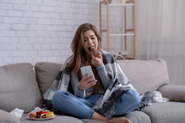Emotional eating concept. Upset young woman with sweet pastry looking at smartphone, waiting for...