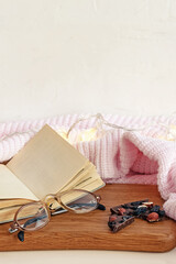 Flat lay composition with open blank paper notebook glasses and natural black chocolate bar with nuts and dried fruits near white knitted blanket and fairy lights.