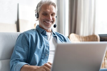 Smiling man in headset watch webinar or training on modern computer, male call center agent or...