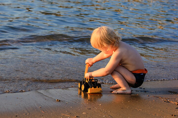 Little boy playing on the beach with a toy car. Summertime, vacation, travel, childhood concept.